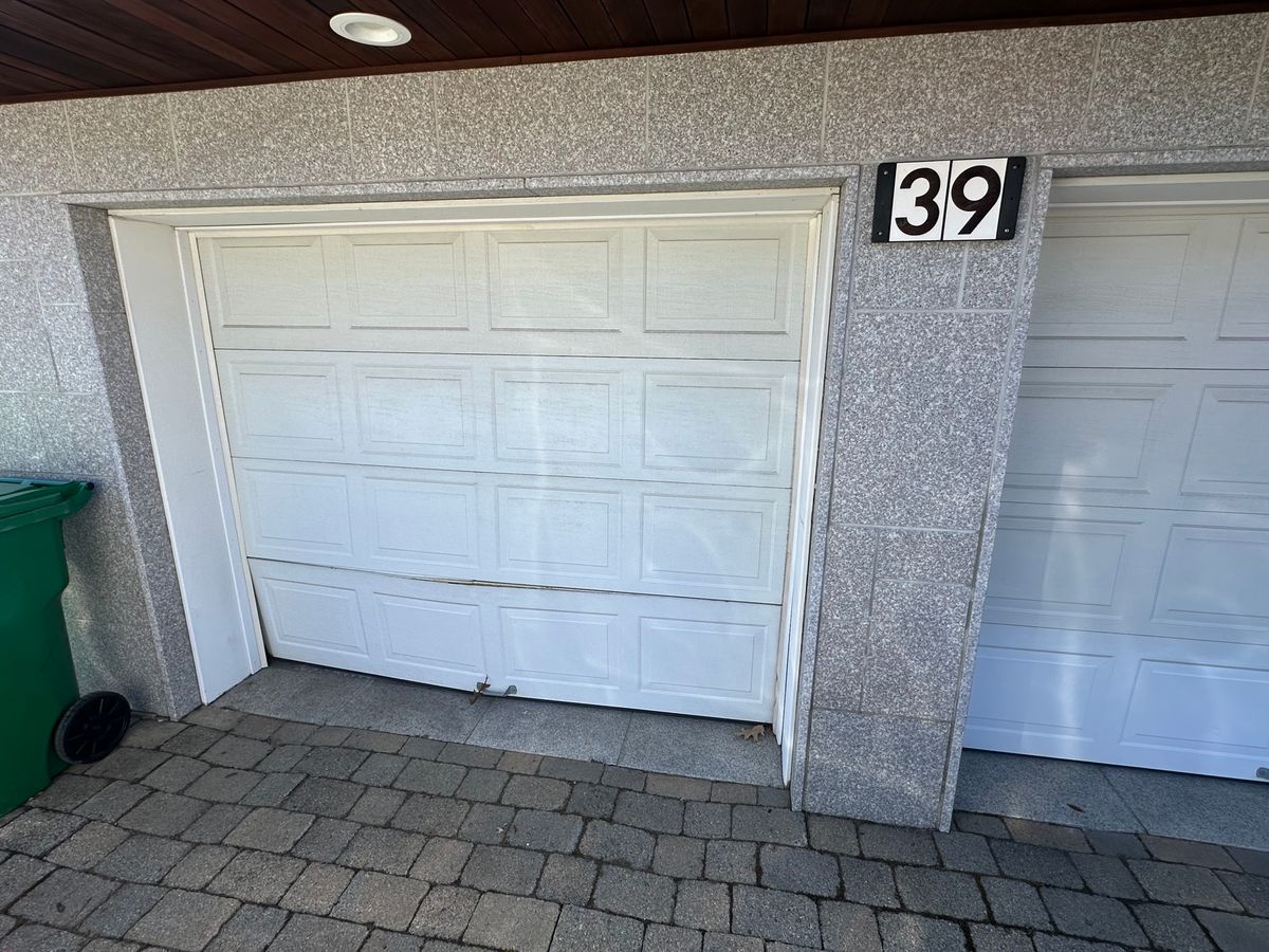 Damaged and misaligned white garage door panel needing replacement